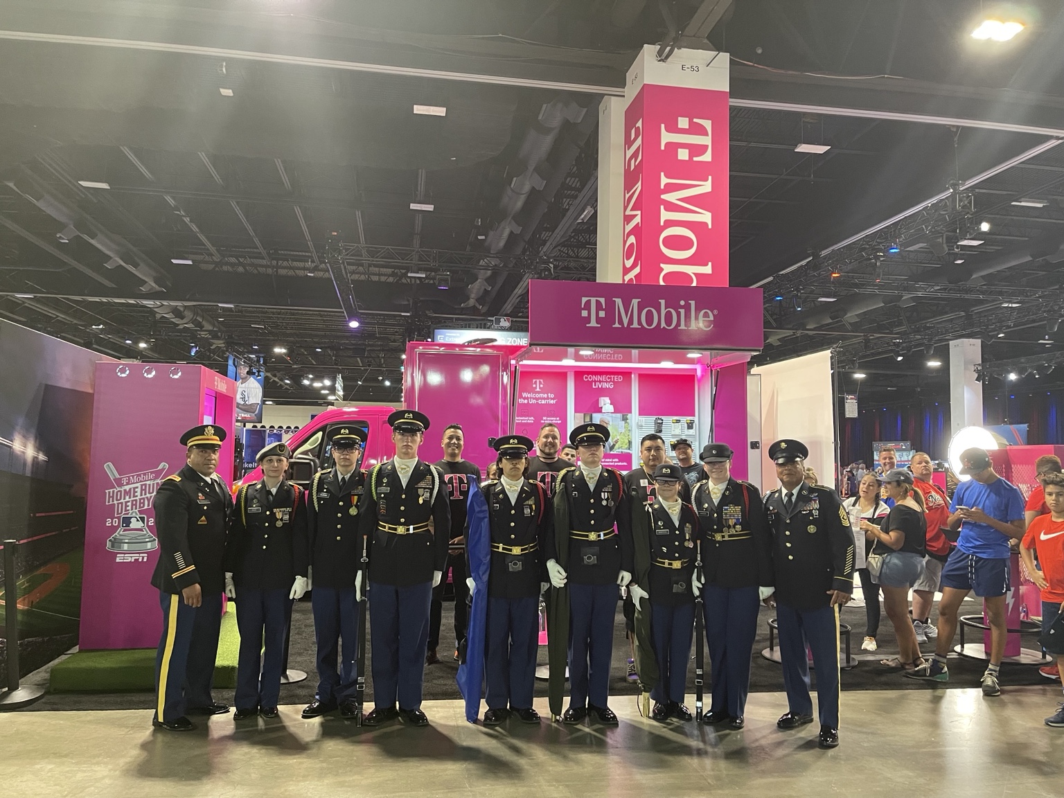 Uniformed guests and T-Mobile team members pose together in front of a magenta mobile activation at an indoor fan event