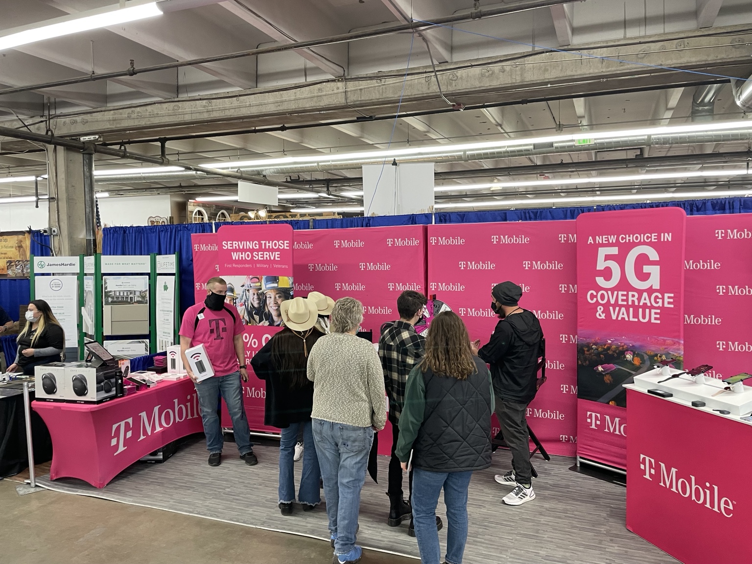 Visitors speak with T-Mobile staff at an indoor event booth with product demonstrations and magenta displays